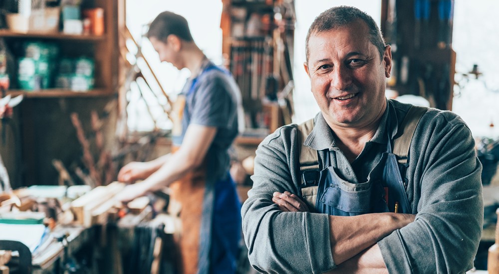 Happy carpenter standing by pick-up truck outside workshop